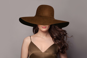 Brunette woman with wavy hair in wide brown broad brim hat.