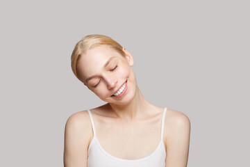 Fototapeta premium Cute woman with blonde ponytail smiling isolated on grey background. Beauty, cosmetics, skincare, glamour