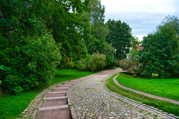 Fototapeta na wymiar Path in green meadow and trees in Park Mon Repos, Vyborg, Russia