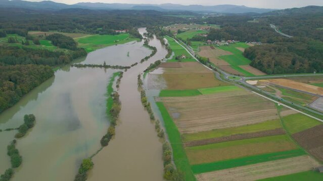 AERIAL: Stunning view of greatly increased river water level flooding rural area. Muddy flood water spilling over river banks after heavy rainfall in autumn and covering grassland, fields and forest.