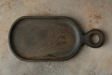 Empty dark brown wooden cutting board over beige stone background. Flat lay composition. Copy space.