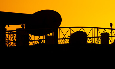 House roof silhouette with satellite dishes at sunset.