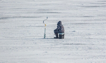 A man is fishing on the ice in winter