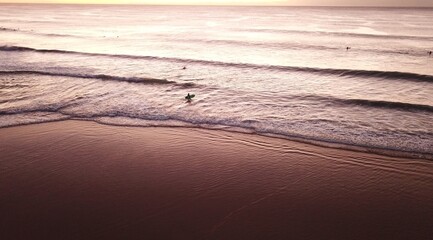 Majestic ocean sunrise with solo surfer walking in to water