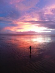 Fototapeta premium Girl walking on a beach in western England at sunset aerial drone