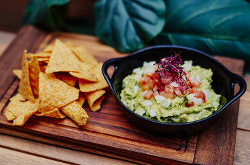 Mexican guacamole with nachos chips on wooden board