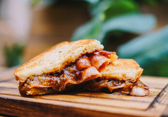 Breakfast sandwich with bacon, cheese and tomato sauce on wooden board