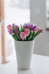 Fototapeta na wymiar A bouquet with tulips of delicate shades in a white vase on the table.