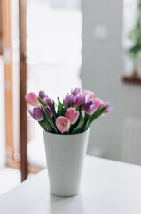 Fototapeta na wymiar A bouquet with tulips of delicate shades in a white vase in the room.
