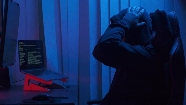 Hacker in hood cracking code using laptop from his dark hacker room