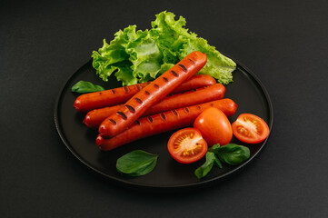 Grilled sausages on a black plate. Vegetables and sauce.