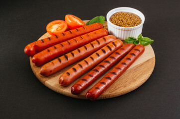 Grilled sausages on a wooden board. Vegetables and sauce.