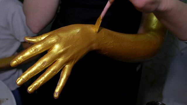 Model girl paints her hand with golden paint.
