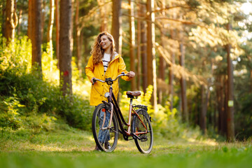 Young woman in yellow coat riding bicycle park. Active day. 
