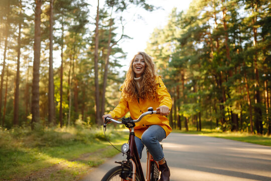 Young woman in yellow coat riding bicycle park. Active day. 