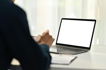 Back view of man worker sitting at office desk with blank screen laptop computer on foreground
