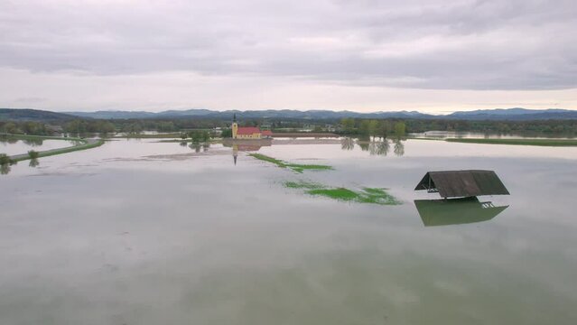 AERIAL: Village church in the middle of a large flooded area after heavy rainfall. Flooded countryside after river's muddy floodwaters spilled over river banks and inundated meadows, fields and forest
