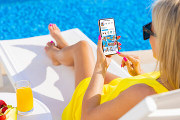 Woman viewing social media app on mobile phone while relaxing by the pool
