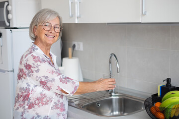 Smiling senior woman drinking tap water from glass in kitchen