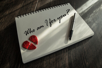 Tekst: Who am I for you napisany piórem na karcie brulionu, na którym leży pęknięte czerwone...