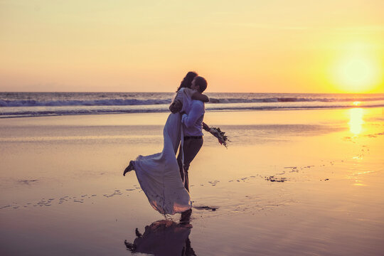 Newlywed couple embracing at beach against clear sky during sunset - Powered by Adobe