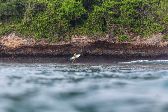 Distant view of man with surfboard walking at beach by mountain
