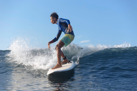 Side view of boy surfing on sea against blue sky