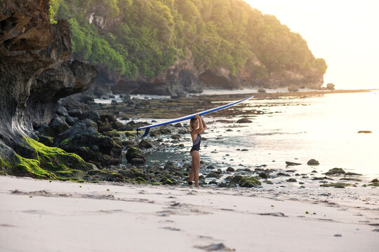 Side view of woman carrying surfboard on head while standing at beach