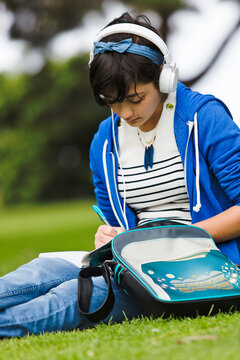 Teenage girl listening music while writing on journal at park