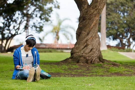 Teenage girl writing on journal while listening music at park