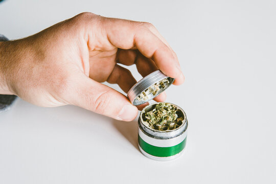 Cropped hand of man grinding marijuana in metallic grinder on table