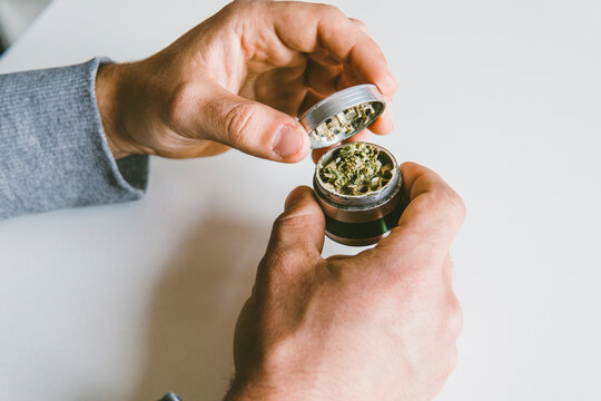 Cropped hands of man grinding marijuana in metallic grinder over table at home