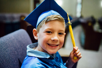 Portrait of happy boy in graduation gown siting on chair