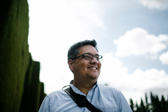 Smiling tourist wearing eyeglasses while looking away against cloudy sky
