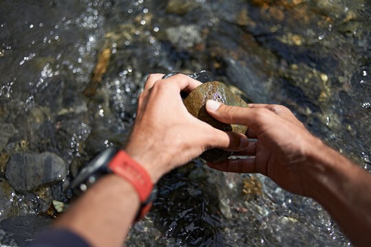 Cropped hands of hiker picking rocks from flowing river