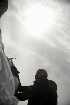 Low angle view of hiker using ice axe while climbing mountain against sky during winter