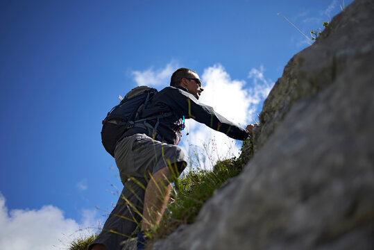 Low angle view of hiker climbing mountain against sky during sunny day