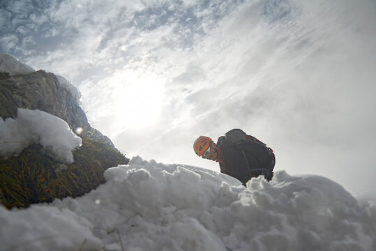 Low angle view of hiker on snowcapped mountain against cloudy sky during winter