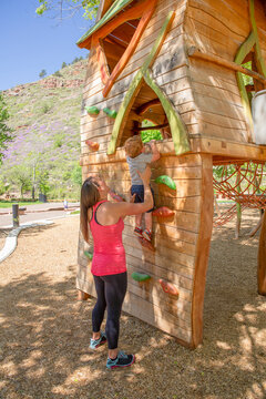 Full length of mother helping son in climbing on wooden wall at playground