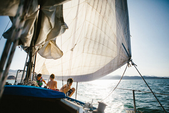 Kids sit on sailboat while sailing on lake in swimsuits summer
