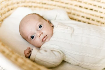 Fotobehang Baby mit großen Augen in weißem Overall in Moseskorb in naturfarben © freudelachenliebe