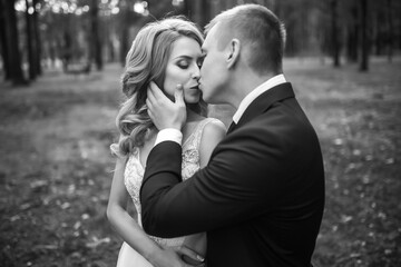 Stylish couple of happy newlyweds posing in the park on their wedding day. Perfect couple bride, groom posing and kissing. 