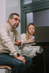 Obraz premium Middle-aged male person thinking about solution for their project problem while his blonde female coworker is chatting on her phone