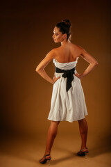 Naklejka premium A back view of a girl posing in white dress with black belt and high heels