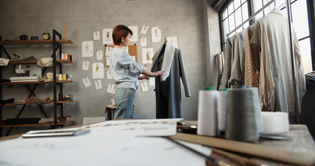 Hipster female fashion designer working with clothes on mannequin in her office, picking the best option for her customers - fashion, small business concept 