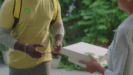 Cropped shot of recognizable delivery man giving two pizza boxes to female customer while bringing food order at home