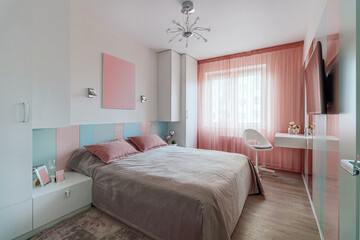 A modern bedroom in blue, pink and white colors with muffled lighting. Real photo