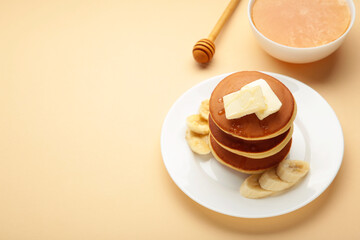Plate with yummy banana pancakes on beige background. Space for text