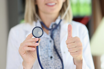 Woman cardiologist holding stethoscope and showing thumb up gesture.