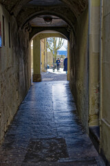Obraz premium Distant view of senior gray haired woman walking through narrow passage at the old town of Swiss City of Bern on a sunny winter day. Photo taken February 21st, 2023, Bern, Switzerland.